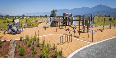 A silver playground on wood chip surfacing with purple flowers bordering it