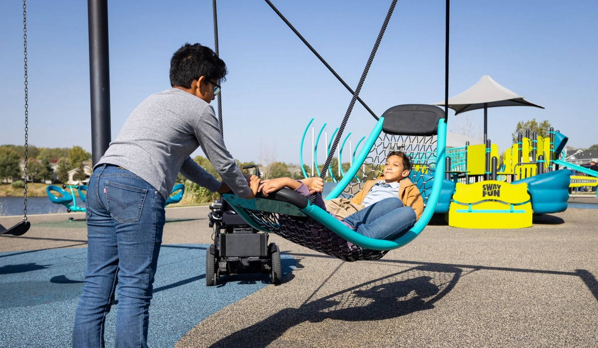 One boy pushing two others in a hammock like swing